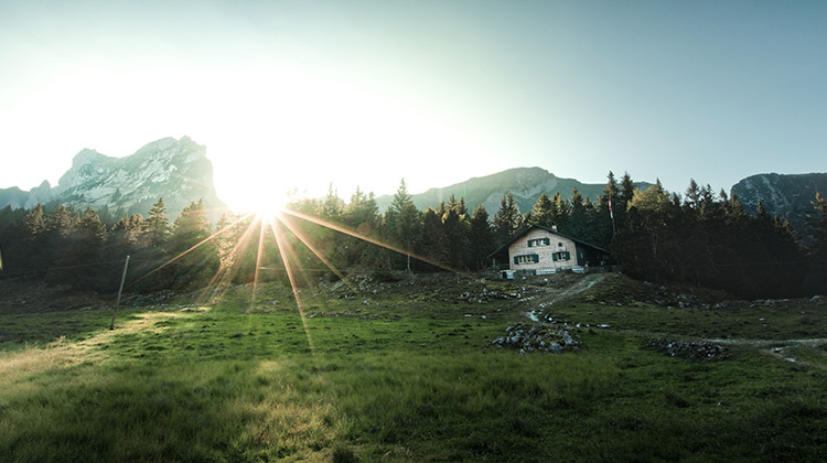 Sun shining through mountains over a pasture